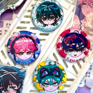 Op de afbeelding: Een verzameling kleurrijke anime-stijl karakterknopspelden. Elke speld toont een ander personage met unieke haar- en oogkleuren, en sommige hebben accessoires zoals maskers of strikken. De spelden zijn gerangschikt op een witte tray.