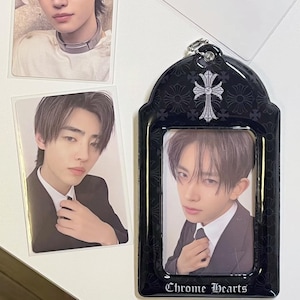 May include: A black photo frame with a silver-colored chain and a cross design, holding a photo of a person in a suit. The frame has the words "Chrome Hearts" at the bottom. Two other photos of the same person are also visible.