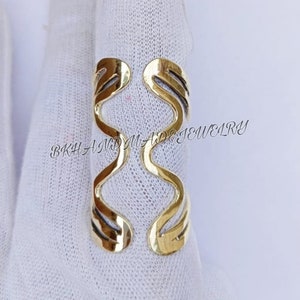 May include: Gold-toned metal ring with a wavy, abstract design. The ring is open and adjustable to fit different finger sizes.