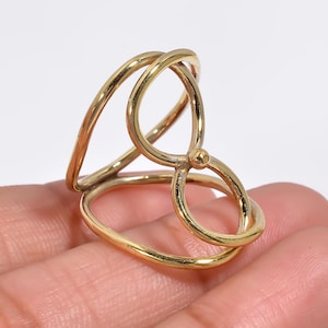 May include: A gold-toned ring with a unique, abstract design. The ring is made of two intertwined bands that form a loop.