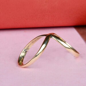 May include: A gold-colored ring with a V-shaped design. The ring is made of two bands that are intertwined.