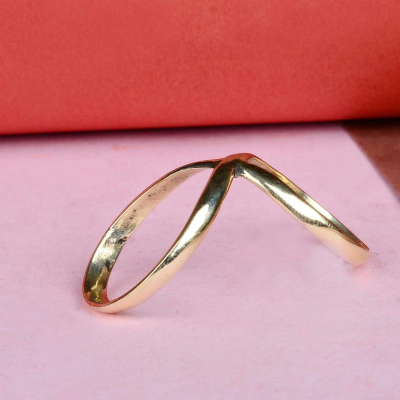 May include: A gold-colored ring with a V-shaped design. The ring is made of two bands that are intertwined.