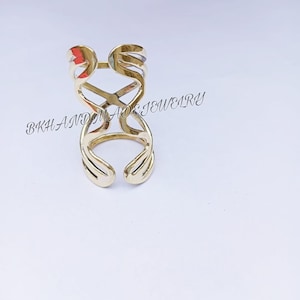 May include: A gold-colored ring with a unique, abstract design. The ring is made of metal and has a delicate, openwork pattern.