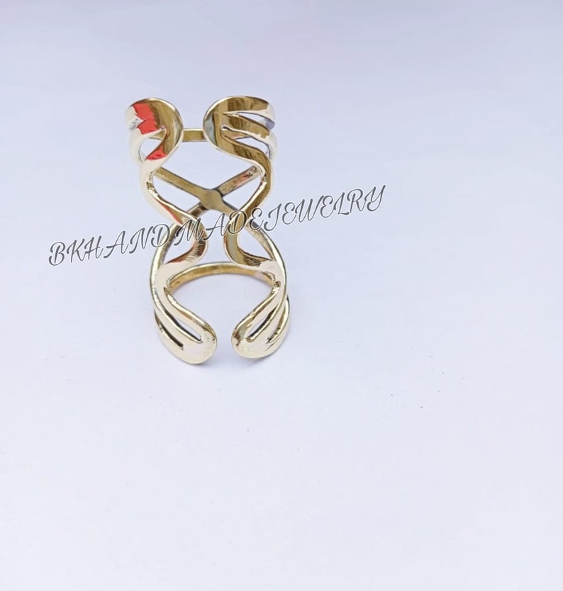 May include: A gold-colored ring with a unique, abstract design. The ring is made of metal and has a delicate, openwork pattern.