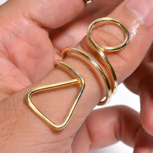May include: Gold ring set with a circle, triangle, and two twisted bands. The ring is worn on a finger.