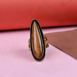May include: A gold ring with a teardrop-shaped tiger's eye stone set in a black bezel.