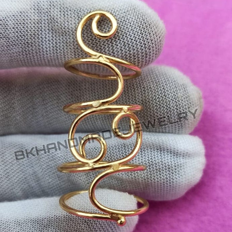 May include: Gold-toned hair ring with a swirling design. The ring is made of wire and has a smooth finish.