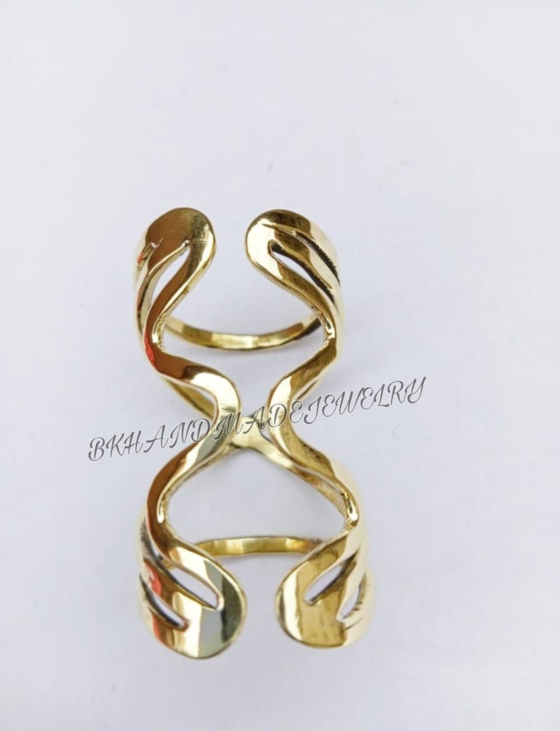 May include: Gold-toned double ring with a unique, abstract design. The ring is made of metal and has a smooth, polished finish.