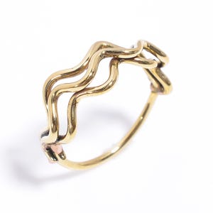 May include: A gold-toned ring with a wavy, abstract design. The ring is made of two intertwined bands.