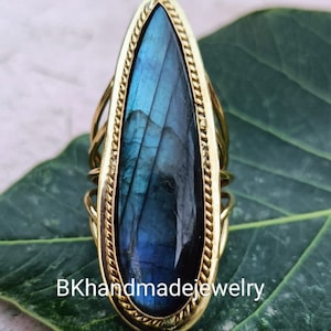 Könnte beinhalten: Ein goldener Ring mit einem großen, tropfenförmigen blauen Labradorit-Edelstein. Der Ring hat ein zartes, gedrehtes Drahtdesign.