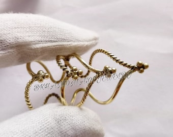 Op de afbeelding: Een gouden, gedraaide draad armband met een decoratief ontwerp. De armband is gemaakt van meerdere draden die met elkaar zijn gedraaid om een uniek en ingewikkeld patroon te creëren. De armband is afgewerkt met kleine, ronde kralen aan de uiteinden.