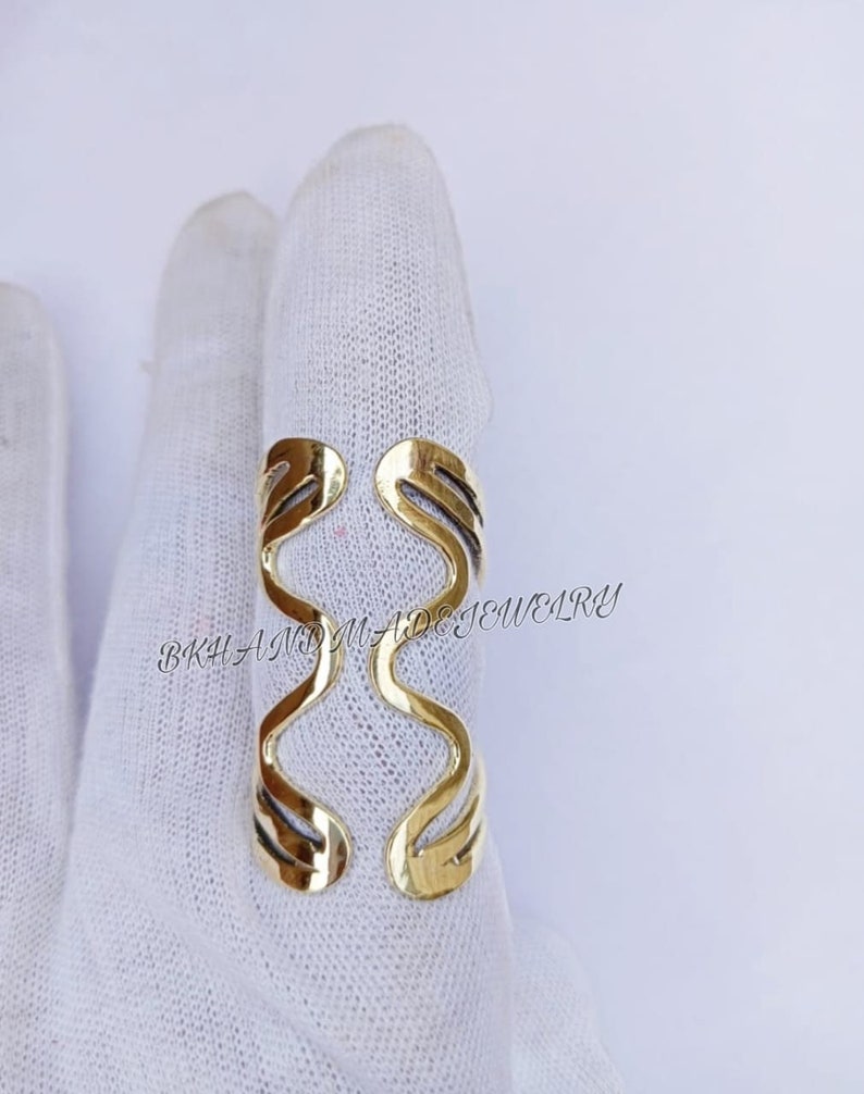 May include: Gold-toned metal ring with a wavy, abstract design. The ring is open and adjustable to fit different finger sizes.