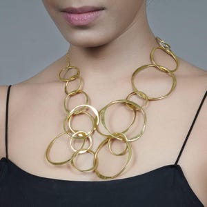 Può includere: Una collana dorata con grandi cerchi intrecciati. La collana è realizzata in metallo martellato e presenta un design moderno e geometrico.