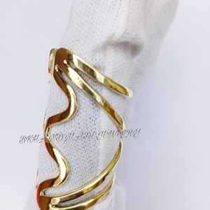 May include: Gold-toned metal ring with a wavy design. The ring is made of multiple bands that are intertwined. The ring is on a white surface. "BKH AND MADE JEWELRY" is written on the surface.