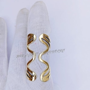 May include: Gold-toned ring with a wavy, abstract design. The ring is made of metal and has a polished finish.