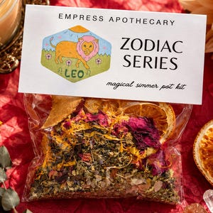 May include: A clear plastic pouch containing a blend of dried herbs, flower petals, and citrus slices. The label reads EMPRESS APOTHECARY ZODIAC SERIES, featuring a hexagonal illustration of a lion and the text LEO, with magical simmer pot kit below.