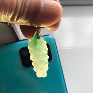 May include: A jade green grape pendant charm with a silver bail. The pendant is made of smooth, polished jade and features a cluster of grapes.