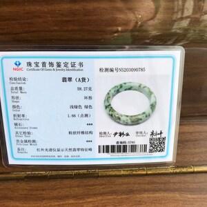 May include: A jadeite jade bangle with a light green and dark green color. The bangle is 58.27 grams and is certified as type A jade. The certificate includes a QR code for verification.