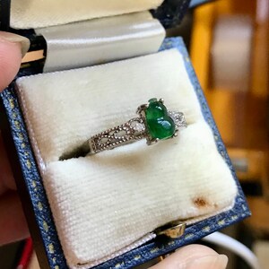 May include: A silver ring with a green jade stone in the shape of a gourd. The ring is set with small diamonds.
