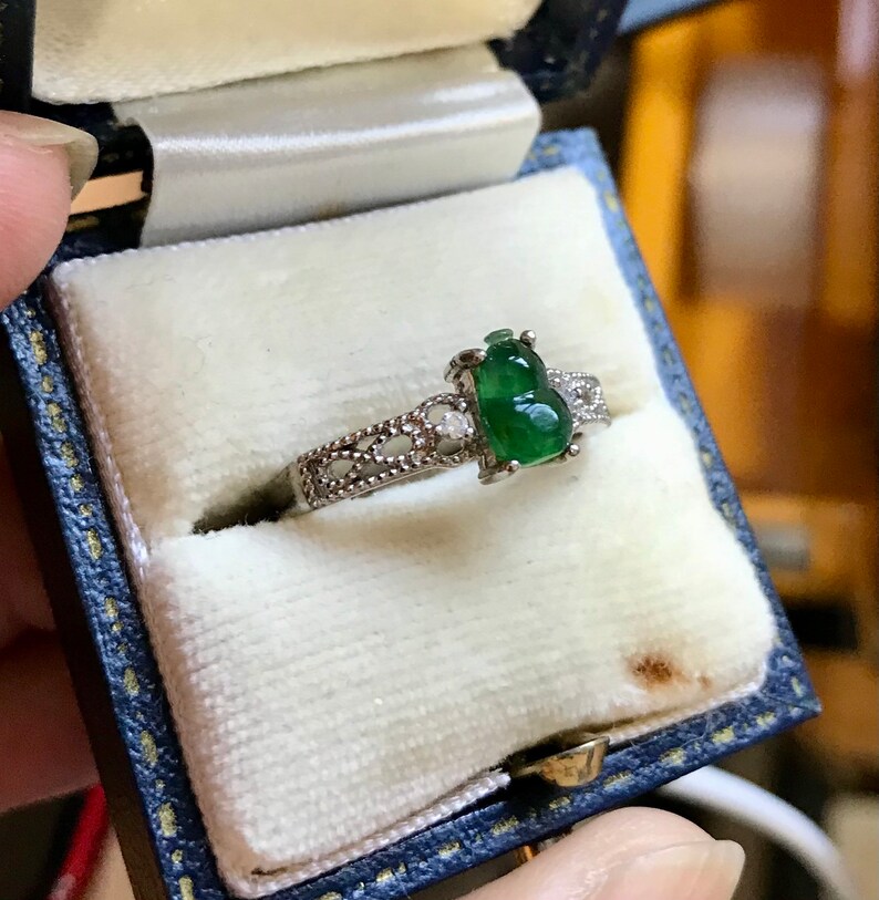 May include: A silver ring with a green jade stone in the shape of a gourd. The ring is set with small diamonds.