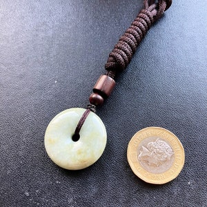 May include: A jade green pendant in the shape of a ring with a brown cord and wooden bead. The pendant is about the size of a British one pound coin.