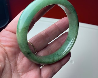 May include: A green jade bangle bracelet. The bracelet is smooth and polished, with a slightly darker green hue on the inside.