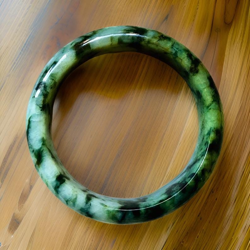 Puede incluir: Un brazalete de jade verde con un patr&oacute;n moteado. El brazalete es liso y pulido.