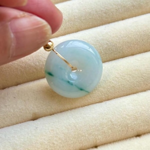 Könnte beinhalten: Ein hellgrüner Jade-Anhänger in Form eines Donuts mit einer goldenen Drahtschlaufe.