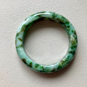 May include: A green jade bangle with a white and green marbled pattern. The bangle is smooth and polished.