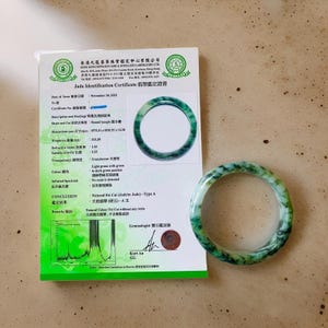 Puede incluir: Un brazalete de jade&iacute;ta de color verde claro y verde oscuro. El brazalete tiene un di&aacute;metro de 14,30 cm y pesa 315,38 gramos. El certificado indica que la jade&iacute;ta es de tipo A y natural, sin resina detectada. El certificado est&aacute; fechado el 30 de noviembre de 2022.