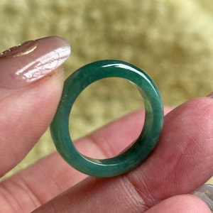 May include: A smooth, circular ring crafted from a solid piece of translucent green stone. The band features a polished, glossy finish with natural variations in color intensity, ranging from deep emerald to lighter shades of seafoam green.