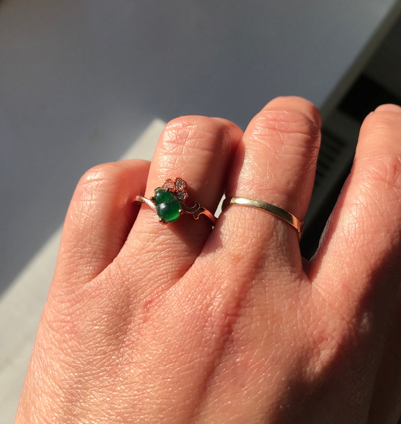 May include: A gold ring with a green gemstone and small diamonds. The ring is on a person's finger.