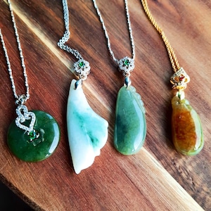 Op de afbeelding: Vier jade hangers aan zilveren en gouden kettingen. De hangers zijn van verschillende vormen en kleuren, waaronder groen, wit en bruin.