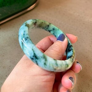Puede incluir: Un brazalete de jade con un patr&oacute;n de m&aacute;rmol verde y blanco. El brazalete es liso y pulido.