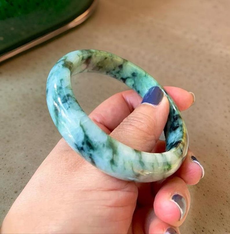 Puede incluir: Un brazalete de jade con un patr&oacute;n de m&aacute;rmol verde y blanco. El brazalete es liso y pulido.