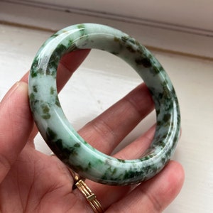 May include: A green jade bangle bracelet with a mottled pattern. The bracelet is smooth and polished.