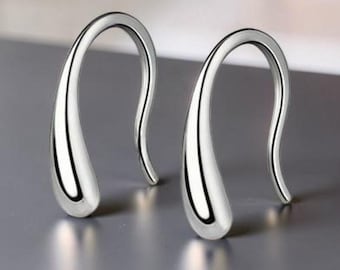 Pode incluir: Um par de brincos de tom prateado com um design liso, curvo e em forma de gota. Os brincos têm um acabamento metálico polido e reflexivo, com uma estrutura de gancho que se estreita na parte inferior de cada peça.
