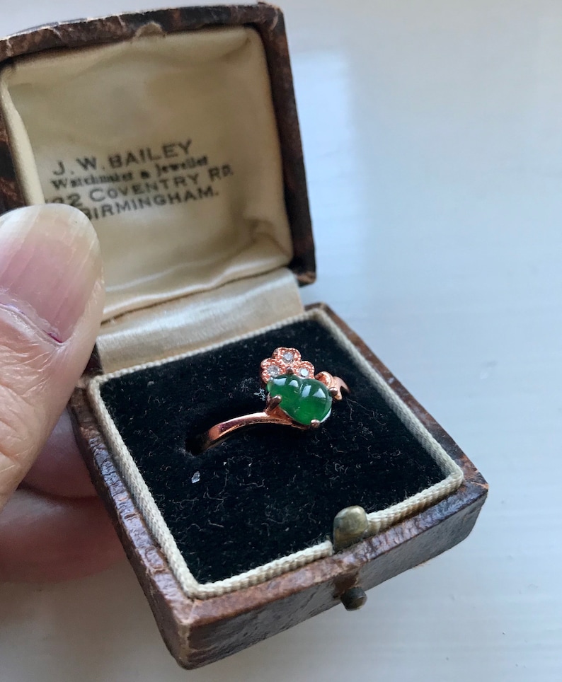 May include: A green jade ring with a rose gold setting and small diamonds. The ring is in a small, brown velvet box with the inscription "J.W. BAILEY Watchmaker & Jeweller 32 COVENTRY RD. BIRMINGHAM."