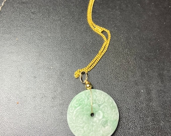 May include: A green jade pendant necklace with a round, carved jade pendant featuring a floral design. The pendant is attached to a gold chain.