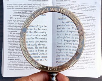 May include: A magnifying glass with a brass frame and a wooden handle. The glass is over a page of text from a book about English literature. The text includes the words "Laying piece of advice" and "Suggestive".