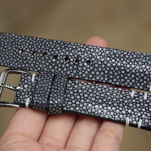 May include: A black and white stingray leather watch strap with white stitching. The strap has a silver buckle.