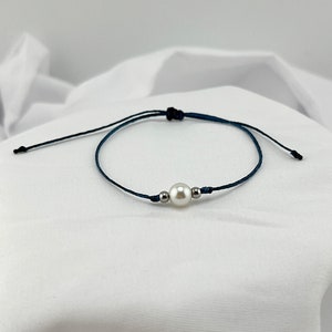 May include: A simple bracelet made with dark blue cord and a single white pearl bead.
