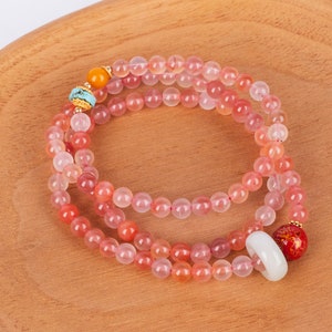 Peut inclure: Un collier de perles composé de pierres précieuses roses et oranges. Le collier comporte des perles dorées, une perle turquoise et une perle orange. Une bague blanche et une perle rouge et or sont également attachées.