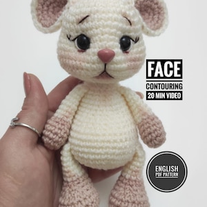 Könnte beinhalten: Ein gehäkelter weißer und rosa Maus-Schlüsselanhänger mit schwarzen Augen und einer rosa Nase. Der Schlüsselanhänger wird in einer Hand gehalten. Der Text "FACE CONTOURING 20 MIN VIDEO" und "ENGLISH PDF PATTERN" ist auf dem Bild zu sehen.
