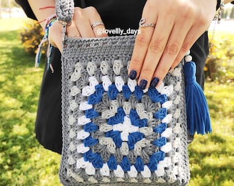 May include: A handmade crochet crossbody bag in gray, white, and blue. The bag features a square granny stitch design with a blue tassel and a gray strap. The text "@lovelly_days" is visible on the bag.