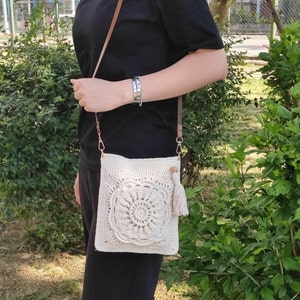 May include: A white crocheted crossbody bag with a tassel. The bag has a circular design in the center.