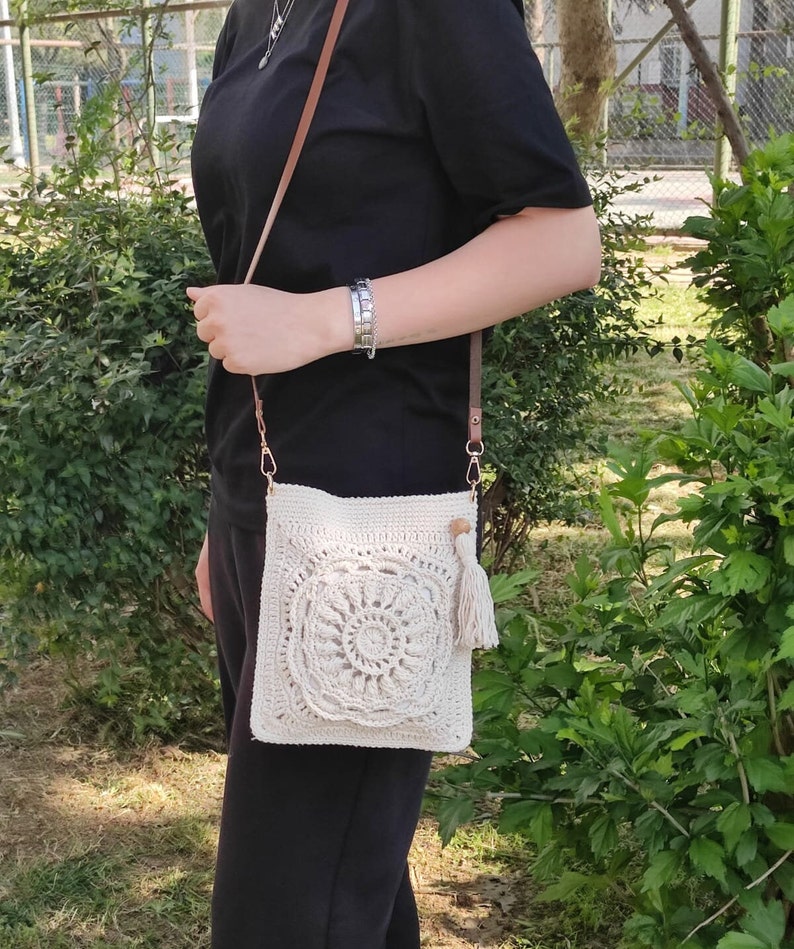 May include: A white crocheted crossbody bag with a tassel. The bag has a circular design in the center.