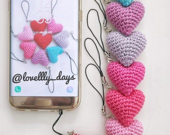 Puede incluir: Encantos de teléfono con forma de corazón de ganchillo en rojo, rosa, morado y azul, sujetos a cordones negros con cierres plateados. Un smartphone muestra un diseño de corazón en su pantalla. También se ve el texto "FREE PATTERN".