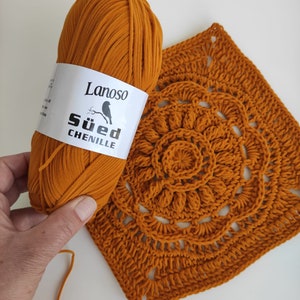 May include: A ball of orange yarn labeled "Lanoso S&uuml;d Chenille" next to a crocheted square with a circular design in the center.
