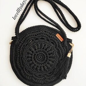 Pu&ograve; includere: Borsa a tracolla rotonda in crochet nero con una catena dorata e un pon pon. La borsa ha un piccolo cartellino in pelle marrone con il testo "lovelydays" su di esso.